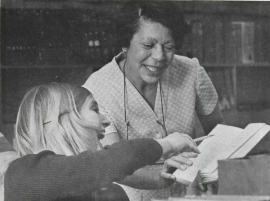 a librarian showing a book to a student who is pointing at one of the pages smiling